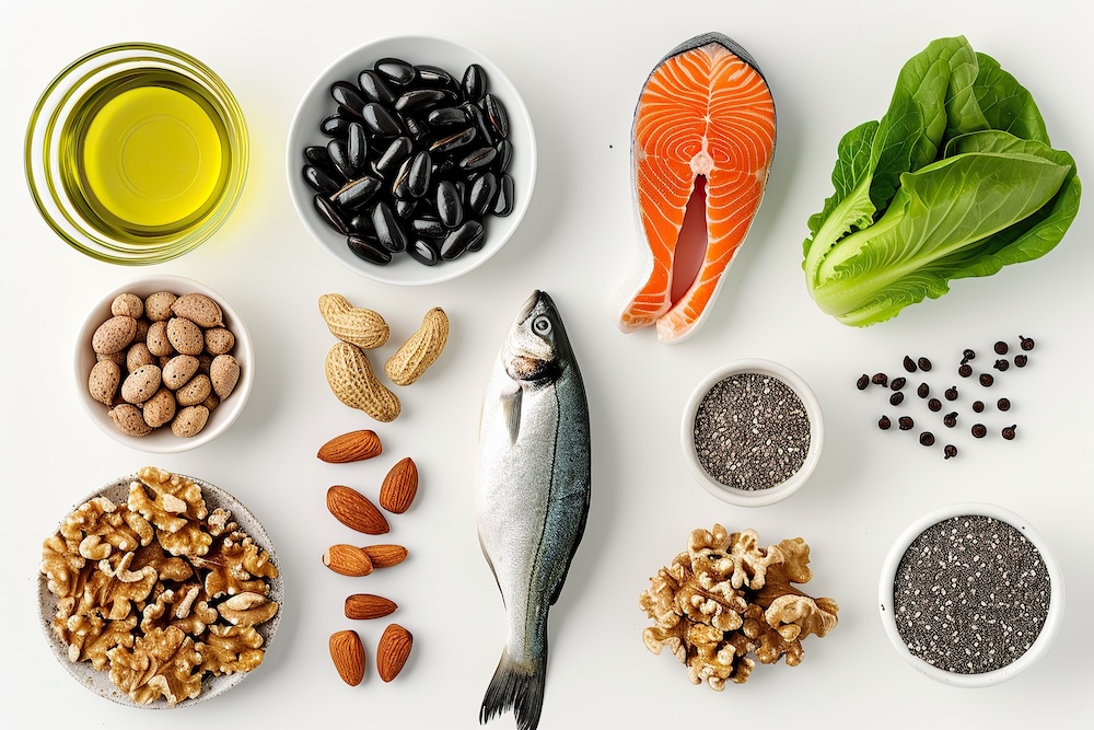 Verschiedene Omega-3-reiche und Omega-6-reiche Lebensmittel auf weißem Hintergrund, darunter Lachs, ganzer Fisch, Walnüsse, Mandeln, Erdnüsse, schwarze Bohnen, Chiasamen, grünes Blattgemüse und ein Glas Olivenöl.