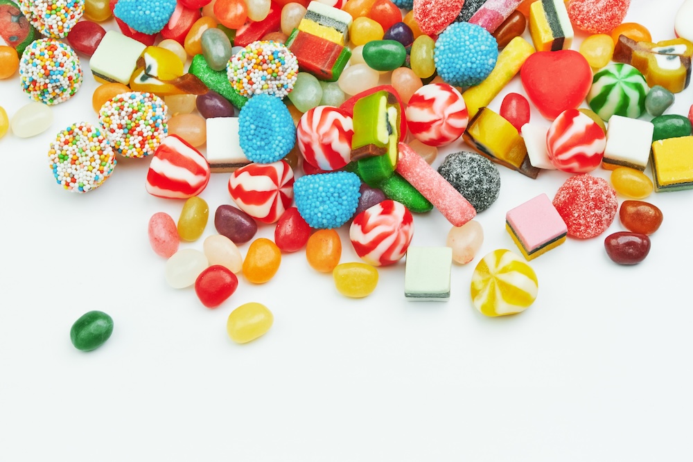 Bunte Mischung aus Süßigkeiten, darunter Gummibärchen, Bonbons, Geleebonbons, Lakritz und Schaumzucker, auf weißem Hintergrund verstreut.
